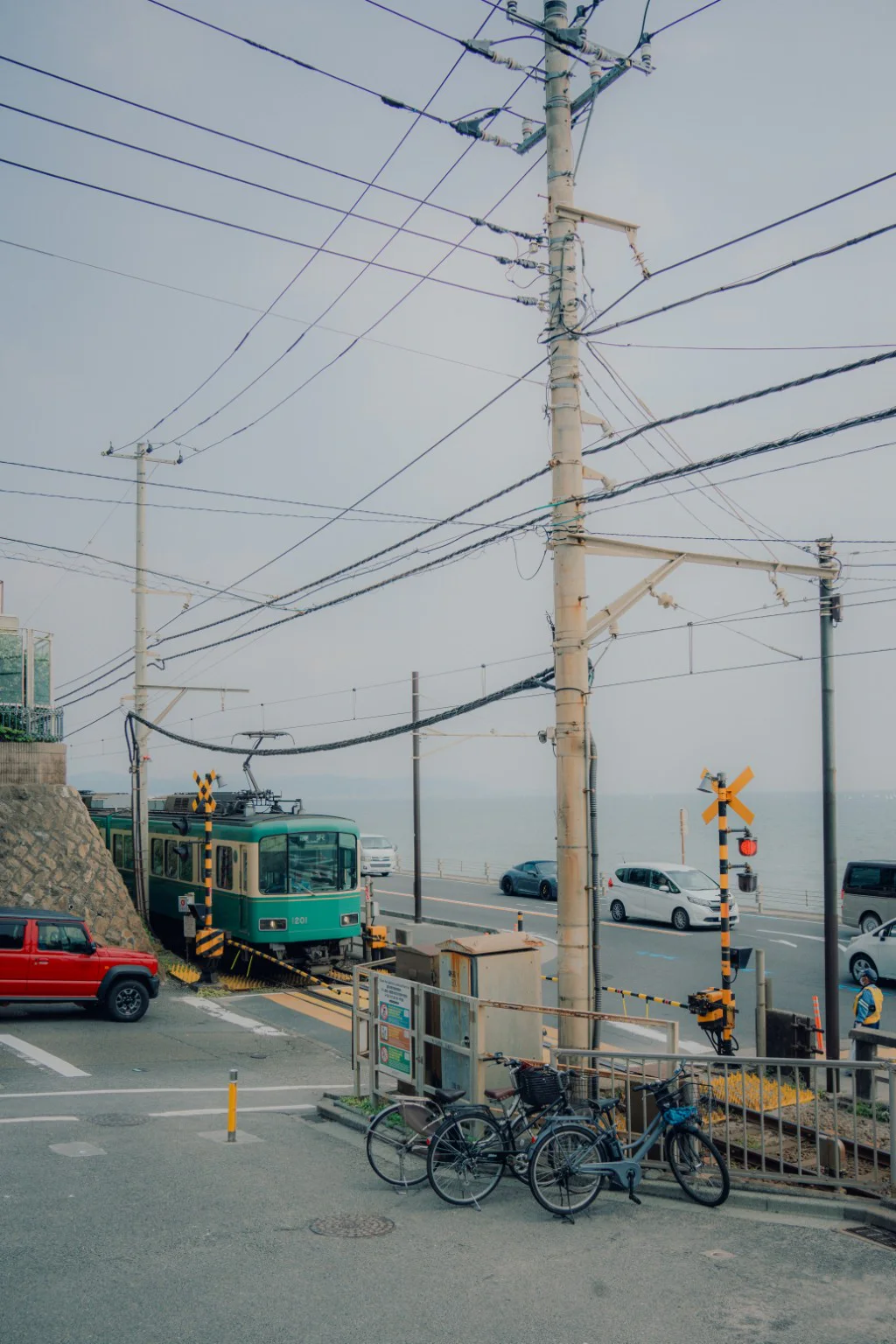 A green train passing a quiet coastal railway crossing